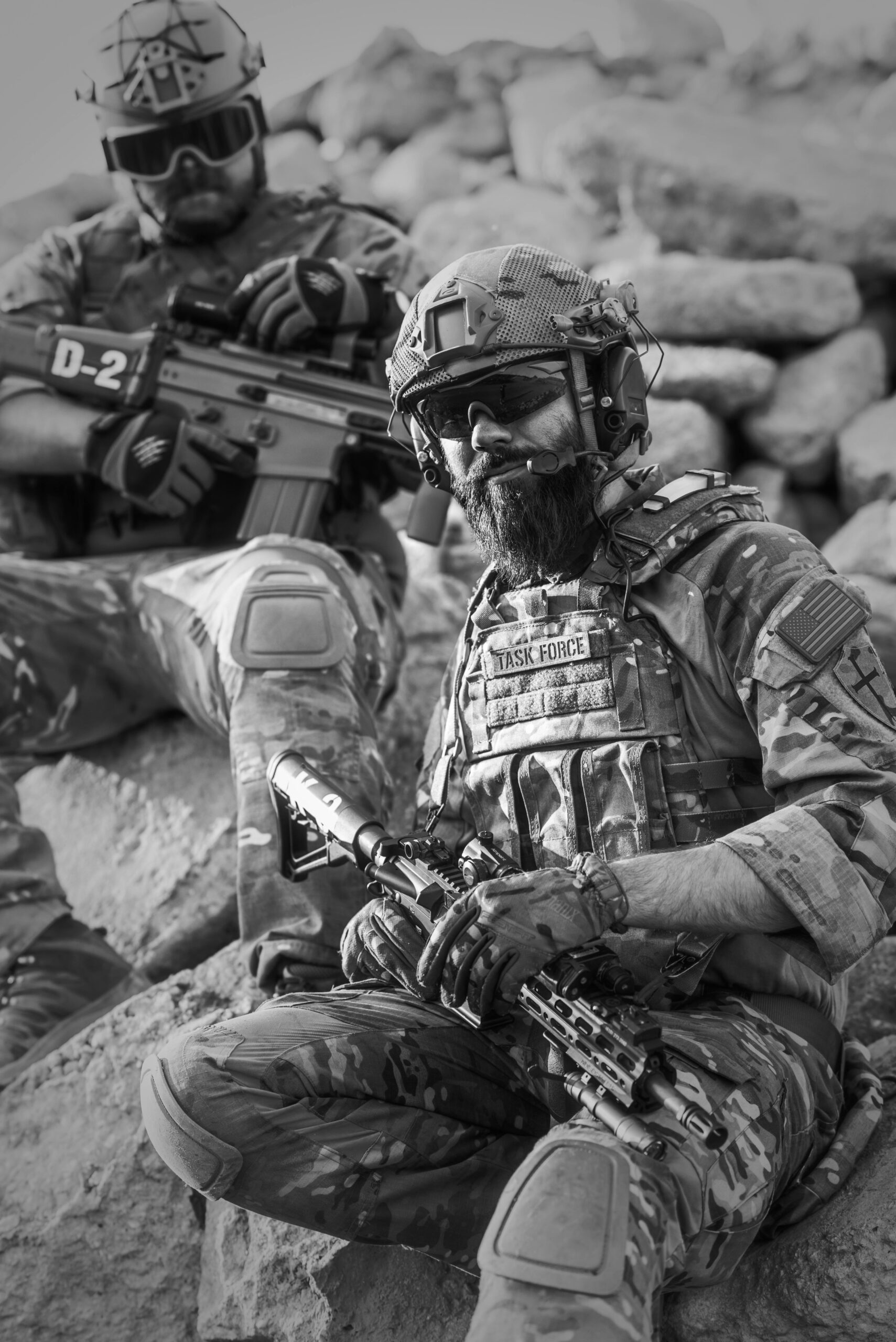 Two soldiers in tactical gear resting on rocky terrain, ready for action.